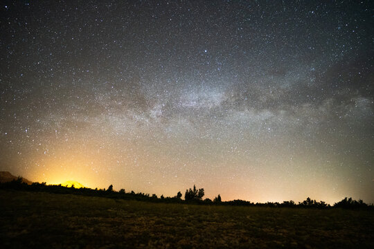 View of the Milky Way galaxy and a starry night sky over a dark landscape with silhouettes of trees and a glowing horizon Jasenice, Zadar County, Croatia.