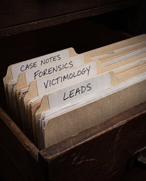 Forensic case files in wooden drawer with victimology leads and notes