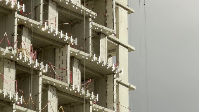 A raw concrete highrise frame stands under an overcast sky during construction. The empty structure creates a stark, cold, and lonely atmosphere.