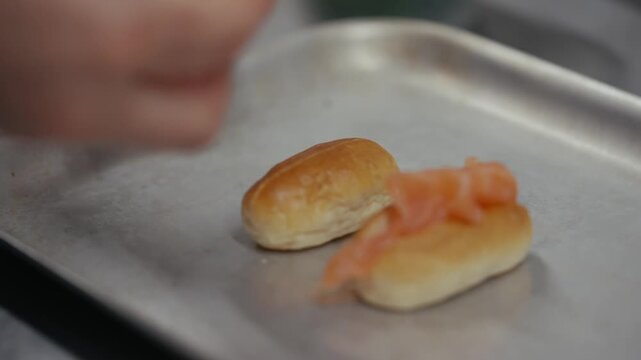 Hands adding smoked salmon to mini brioche rolls on a metal tray