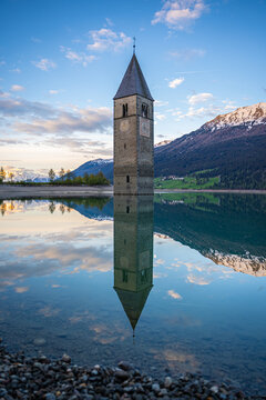 View of Campanile di Curon Venosta Vecchia submerged in Lake Resia with its reflection and snow-capped mountains in the background Curon Venosta, Trentino-Alto Adige, Italy.