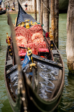 View of a traditional Venetian gondola with ornate red damask upholstery and golden decorations moored in a canal Venice, Veneto, Italy.