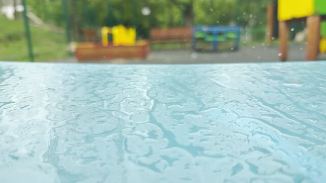 a wet blue swing seat moves slowly in the wind. The motion creates a soft metallic squeaking sound. Water droplets drip quietly from the edge.