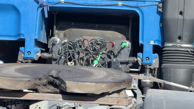 Close view of a blue semi truck fifth wheel coupling and exposed air brake hoses behind the cab, commercial vehicle maintenance, trucking equipment, transport industry.