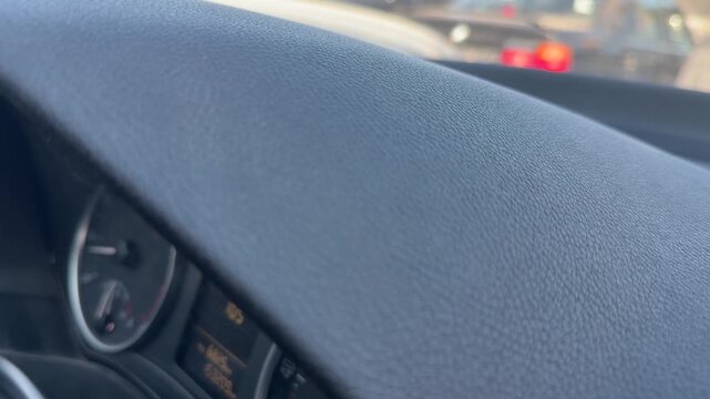 Close-up of a textured car dashboard above the instrument panel while driving in traffic, vehicle interior detail, automotive design, road travel.