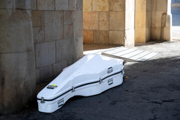 A white hard case for a musical instrument lying on the ground under a stone archway. © elenarostunova