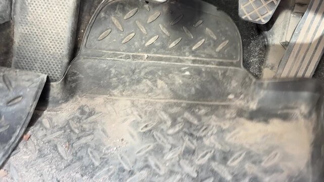 Rubber floor mat is laid flat and aligned around the pedals in a car driver footwell, interior maintenance, automotive cleaning, floor protection.