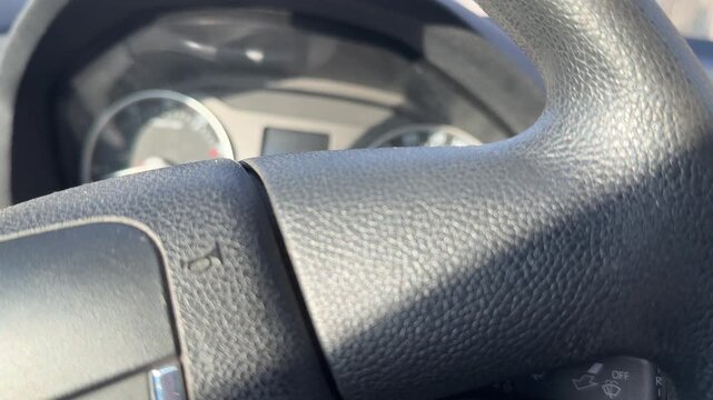 Close-up of the textured center and rim of a car steering wheel with dashboard behind it, horn control, driver equipment, automotive interior.