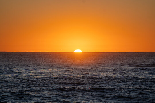 View of the sun setting over the Atlantic Ocean horizon with a vibrant orange sky and dark rippling water El Cotillo, Canary Islands, Spain.