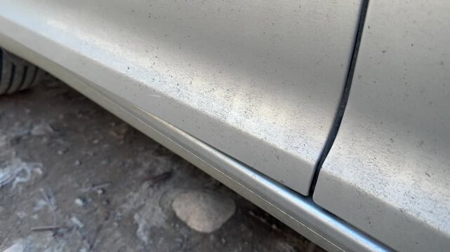 Lower section of a silver car door opens and closes above the rocker panel, vehicle access, exterior body movement, automotive mechanism.
