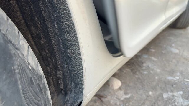 Car door opens and closes beside the front wheel arch, close-up of the silver body panel and dirty tire, vehicle access, automotive movement.