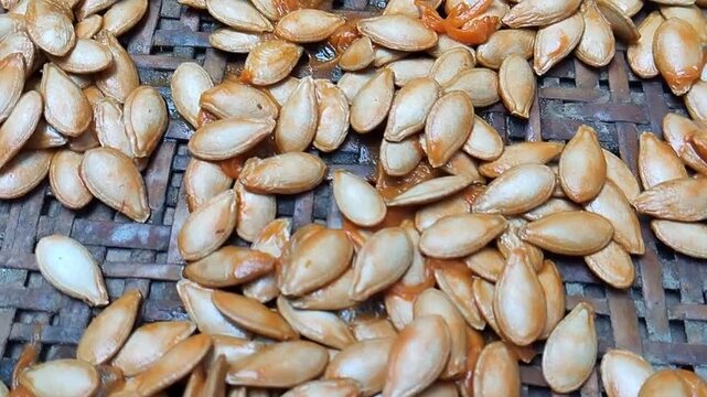 A bunch of fresh organic pumpkin seeds are dried on a traditional woven bamboo tray.