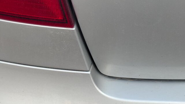 Silver car trunk opens and slams shut beside the rear taillight, close-up of the moving lid and hinge area, cargo access, automotive operation.