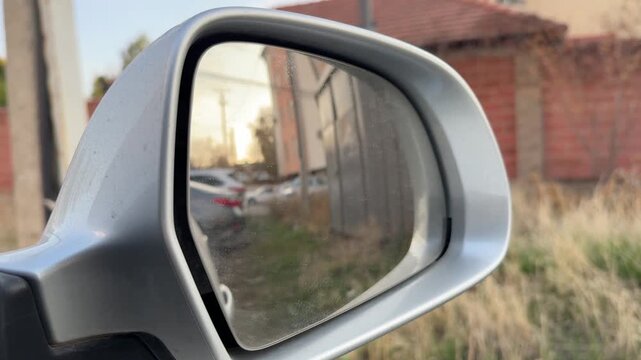 Electric side mirror adjusts its viewing angle on a silver car, powered mirror movement, rear visibility, driver control, automotive safety.