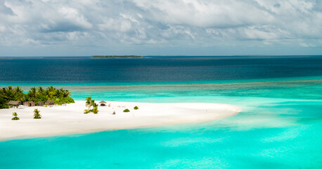 Fototapeta premium Aerial view of a Maldivian atoll sandbank with few palms and shallow turquoise lagoons, deep cobalt waters, tiny uninhabited islet, distant reef line, and bright daylight