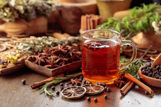 Rustic herbal tea with anise, dried citrus, juniper berries and aromatic spices in a glass mug.