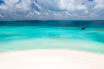 Fototapeta premium White sand arcs into shallow turquoise water deepening to sapphire. A small buoy sits offshore. Low islands line the horizon under soft daylight and cumulus clouds.