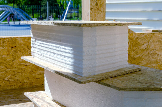 Stacked white foam insulation panels and OSB boards at construction site. These materials are used for SIP panel frame house construction. Proper storage ensures quality building materials.