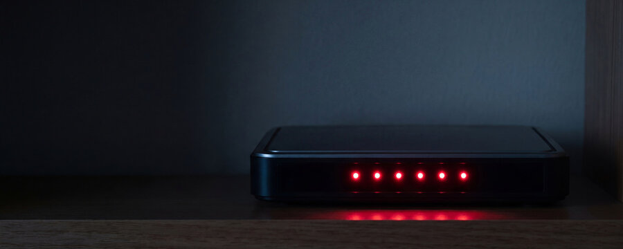 Wi-fi router with red warning lights on wooden shelf. Internet access restriction and connection error concept. Digital security blackout and social media blocking network failure.