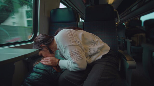 Mother embraces toddler after minor bump on train kissing head to comfort pain conveying protection affection healing care and emotional safety during everyday family commute