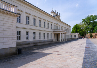 The facade of a historic white palace with multiple windows set against a gravel forecourt in Herrenhausen Gardens, Hannover, Germany. © steheap