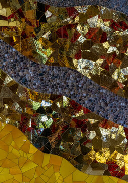 Abstract mosaic art featuring irregular pieces of gold and reddish glass, interspersed with bands of small, gray pebbles, in Herrenhausen Gardens.