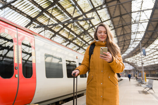 Woman Checks Phone at Train Station With Luggage