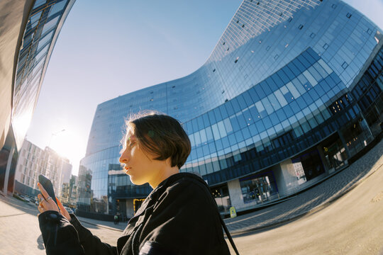 Woman Using Phone Outside Modern Building During Sunny Day