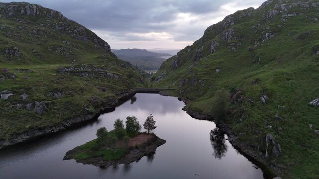Aerial drone captures a push forward movement over the Silver Walk hiking trail. A hiker walks on a small path behind a water dam. Set on the west coast of Scotland, UK on a the spring afternoon.