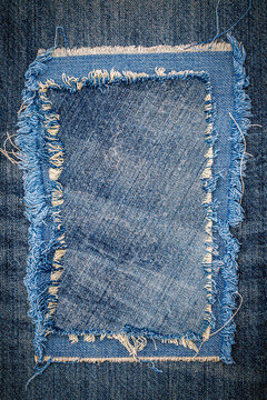 Denim fabric patch placed on blue jean background showing texture and wear in a textile setting