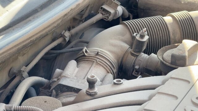 Older gasoline engine runs with visible vibration beneath the hood, close-up of intake hoses and mechanical components, vehicle diagnostics, repair and service.