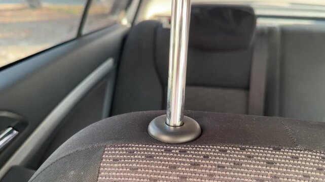 Front car seat headrest moves upward and downward along chrome support rods, adjustable seating position, passenger comfort, vehicle interior, automotive ergonomics.