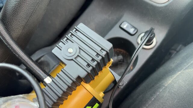 Portable electric air compressor operates inside a car while connected to the power socket, tire inflation equipment, roadside maintenance, automotive emergency tool.