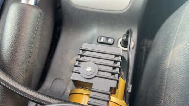 Portable electric air compressor operates inside a car while connected by hose, tire inflation equipment, roadside maintenance, automotive emergency service.