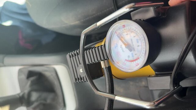 Pressure gauge on a portable car air compressor moves during tire inflation, air pressure monitoring, roadside service, automotive maintenance equipment.