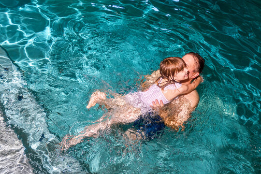 A young girl jumps on her father in a swimming pool