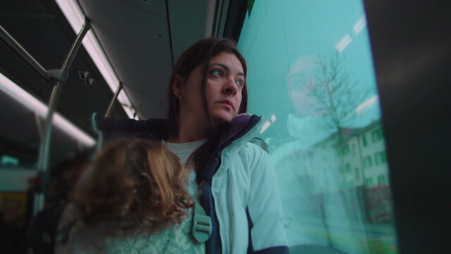 Mother standing by bus window carrying toddler in front carrier during commute evoking responsibility reflection multitasking and calm presence in everyday urban travel