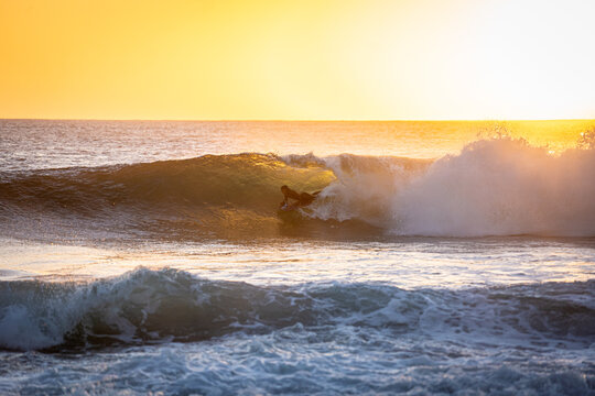 View of a surfer riding inside a breaking barrel wave during a vibrant golden sunset over the Atlantic Ocean El Cotillo, Canarias, Spain.