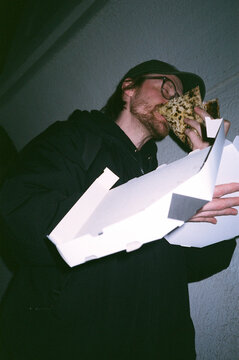 Man enjoys pizza while holding a takeout box
