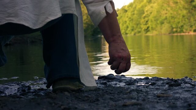 Woman by riverside throws stone into water