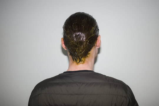 Person with wet dyed hair stands against a plain wall