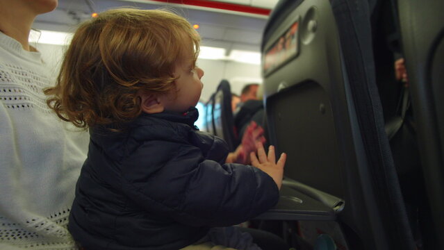 Toddler seated on caregiver lap on airplane reaching toward seatback with curiosity evoking exploration learning trust and early flight experience