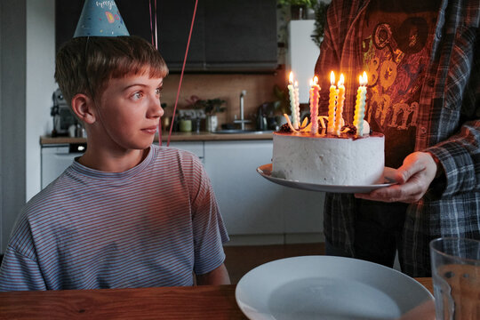 Boy receiving birthday cake with lit candles and party hat
