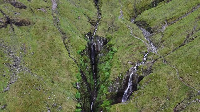 A push forward drone shot reveals a dramatic waterfall cascading into a deep gorge close to Bidean nam Bian and the Three Sisters  in the scottish Highlands, UK.
