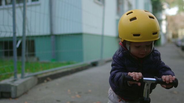 Toddler riding scooter on residential street wearing helmet exploring neighborhood with confidence independence balance childhood adventure urban family lifestyle
