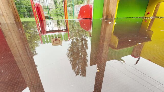 large puddles flood a colorful playground platform. Walking through the water creates a wet splash sound. The empty space gives a lonely and quiet feeling.