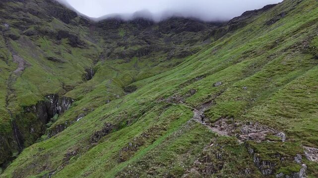 Aerial push forward, boom up view of a hiker approaching Stob Coire Sgreamhach part of Bidean nam Bian and the Three Sisters in the scottish Highlands, UK.