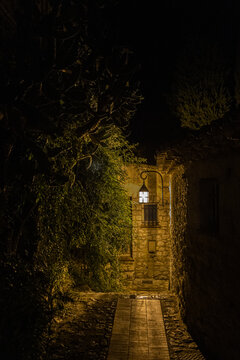 View of a narrow stone alleyway at night with a glowing lantern on a rustic wall and lush greenery in the historic Eze Village Eze, Provence-Alpes-Cote d'Azur, France.