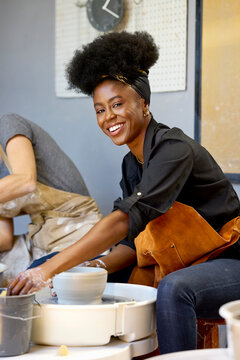 A woman smiles while shaping clay on a potter's wheel