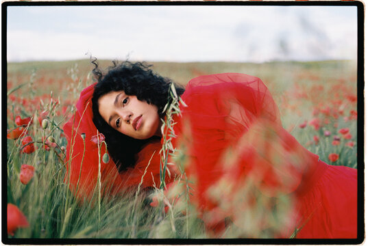 Woman resting in red tulle dress in poppy field